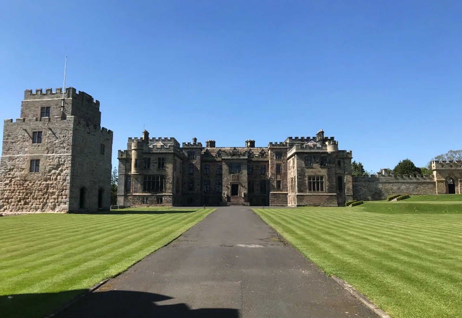A castellated estate house approached by a straight drive across mown lawns
