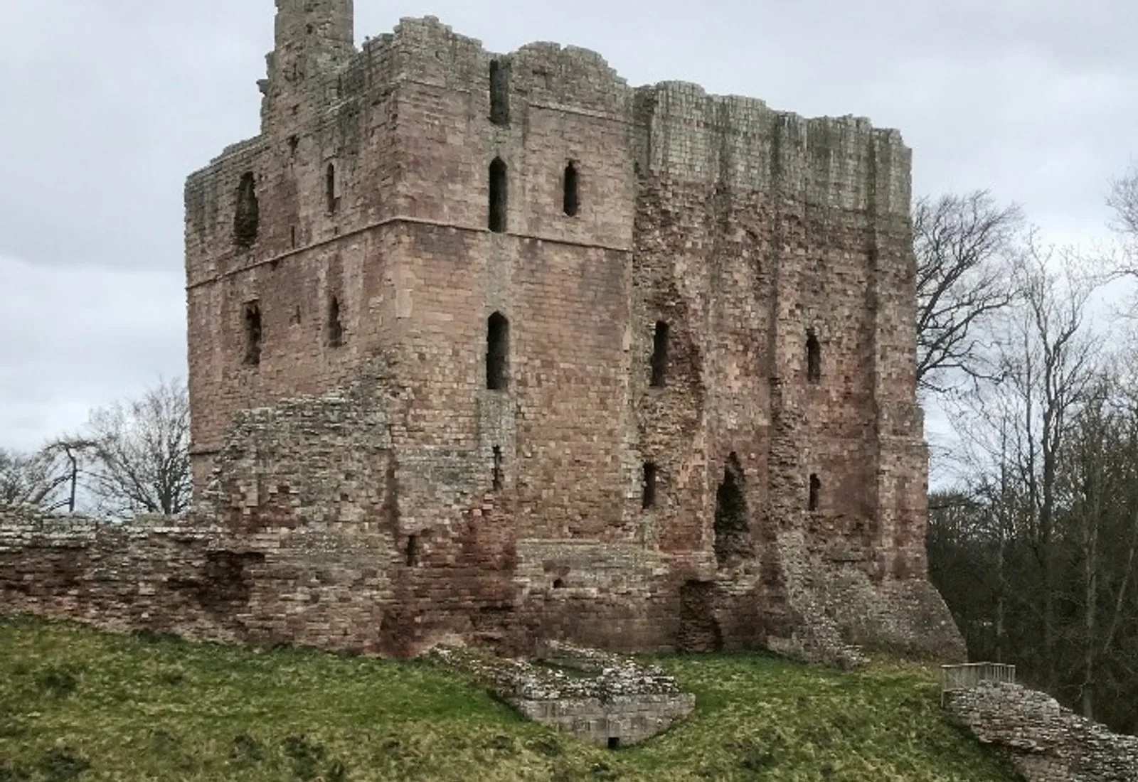 The red sandstone keep of Norham Castle standing above grassland